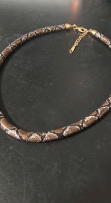 Colar Cobra Ônix sobre uma mesa, mostrando o fecho dourado